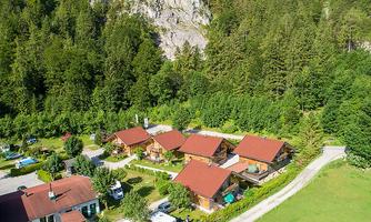 A picturesque holiday resort with several wooden houses surrounded by dense trees. The green lawn and the quiet surroundings provide a relaxed atmosphere.