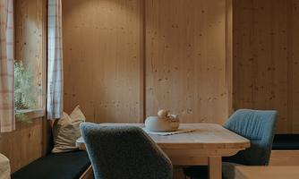 A cozy room with wooden paneling, a dining table, and chairs. The windows let in plenty of daylight and create an inviting atmosphere.