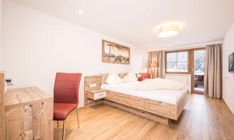 A modern bedroom with a large bed and wooden furniture. The friendly atmosphere is complemented by daylight and elegant decor.
