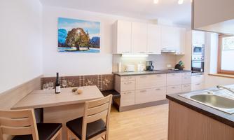 A modern kitchen with a small table and chairs. A picture of a landscape hangs on the wall.