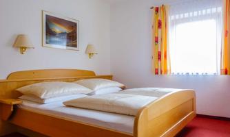 A cozy bedroom with a large wooden bed and bright cushions. The walls are painted in soft colors, and the window lets in plenty of daylight.