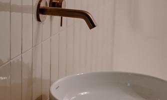 A modern bathroom with a round sink and a stylish faucet. In the background, a round mirror can be seen.