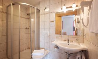 A modern bathroom with a shower and a sink. The walls are tiled with light tiles and there is a large mirror.