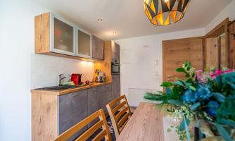 A modern kitchen with wooden furniture and an inviting dining area. The space is brightly lit and offers a cozy atmosphere.