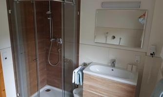 A modern bathroom with a glass shower and a wooden sink. The ambiance is bright and clean, with towel-hanging details.