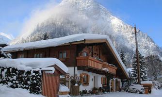 A cozy house in the snow, surrounded by mountains. The landscape radiates peace and winter idyll.