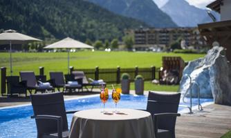 A beautiful outdoor area with a pool and a relaxing atmosphere. At the table, there are two cocktails, surrounded by a picturesque landscape.