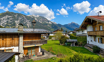 A picturesque landscape with traditional alpine houses and green meadows. In the background, majestic mountains rise under a clear blue sky.