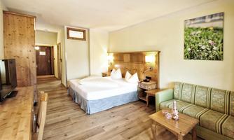 A cozy hotel room with two single beds, a television, and a small table. The walls are painted light, and there is a wooden wardrobe as well as a sofa.