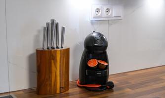 A modern kitchen with a wooden block for knives and a black coffee machine. Visible in the background are outlets.