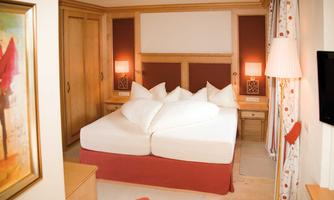 A cozy hotel room with a large double bed and several pillows. The room decor is modern and inviting, featuring wood and color details.