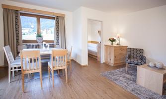 A bright and inviting room with a dining table and chairs. The large windows offer a beautiful view of the mountains.