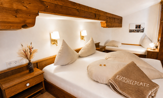 A cozy bedroom with two beds and wood paneling. The pillows and blankets are neatly folded, and the atmosphere is inviting.