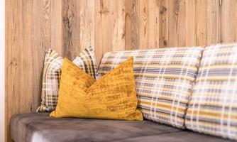 A cozy sofa with striped and checkered cushions in warm colors. The wooden paneling in the background creates an inviting atmosphere.