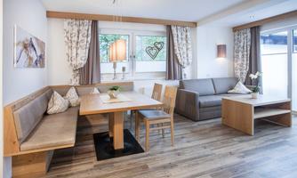 A cozy living room with light wood decor and modern furniture. The space includes a dining table, a bench, and a comfortable sofa.