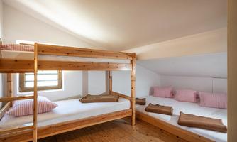 A cozy sleeping room with two bunk beds. The walls are light, and there are bright windows that provide plenty of light.