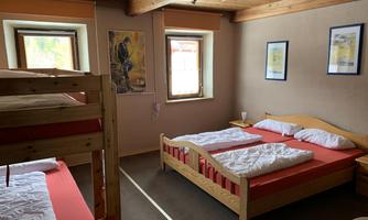 A simple bedroom with wooden beds and two windows. There is a combination of single and bunk beds that look cozy.
