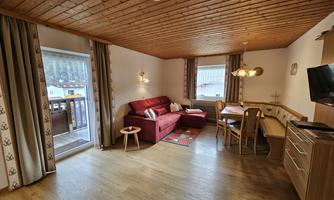 A cozy living room with a red sofa and a dining area. Large windows provide plenty of daylight and a view outside.
