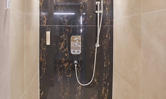 A modern shower featuring elegant dark tiles and a large rain showerhead. The walls are light, and the room is well-lit.