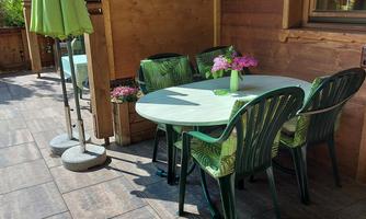 A cozy outdoor area with a round table and green chairs. Fresh flowers are on the table and umbrellas provide shade.