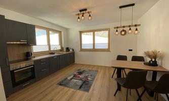 A modern kitchen with wooden details and large windows. The dining area is simply furnished with a table and four chairs.
