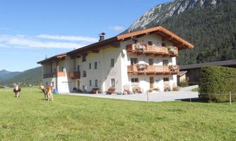 A picturesque farmhouse with a balcony and blooming flowers. In the foreground, cows graze on a green meadow, surrounded by mountains.