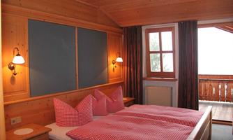 A cozy bedroom with wooden walls and two beds. There are red pillows and access to a balcony with a view.