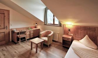 A cozy room with sloping walls and wood paneling. It features a bed, a table, and an armchair.