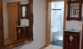 A cozy hallway with a large mirror and a wooden wardrobe. Behind a door, a bathroom with a bathtub is visible.