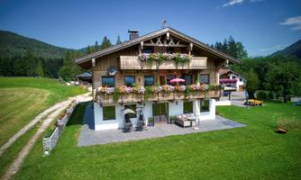 A beautiful wooden house with balconies full of flowers. Surrounded by green meadows and mountains, it offers an inviting view.