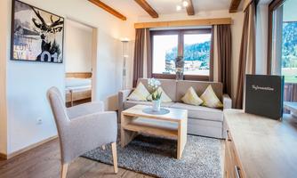 A cozy living area with a sofa, a table, and an artistic wall mural. Large windows offer a view of the mountains and let in a lot of light.