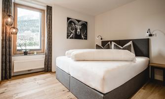 A modern bedroom with a large bed and wooden floor.  
Light-flooded room with a window view of the mountains and a piece of artwork on the wall.