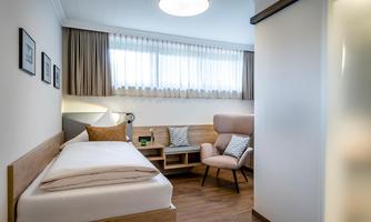 A modern bedroom with a single bed and a cozy armchair. Bright colors and large windows create a friendly atmosphere.