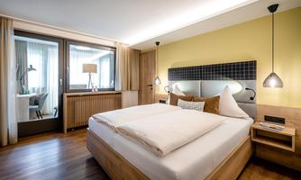 A modern room with a large bed and stylish decoration. The window offers a view of the outdoor area and provides plenty of daylight.