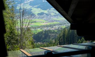 A view of a green landscape with a valley and gentle hills. In the foreground, part of a terrace or building is visible.