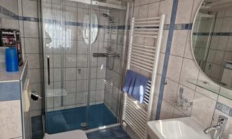 A modern bathroom with a glass shower and wall tiles. There is a sink, a toilet, and towels available.