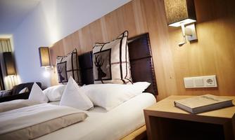 A modern bedroom with a large bed and stylish pillows. The warm wood details and soft lighting create a cozy atmosphere.