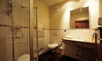 A modern bathroom with a shower, marble sink, and a large mirror. The walls are light, and the floor tiles are dark.