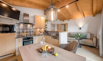A modern kitchen with wooden ceilings and a dining area. The space is bright and inviting, with fresh fruits on the table.