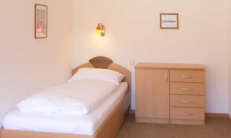 A simple bedroom with a single bed and a wardrobe. The walls are light and there are some pictures for decoration.