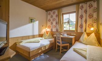 A cozy hotel room with two single beds and wooden paneling. Natural light shining through the window and an inviting atmosphere.