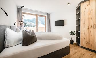 A modern bedroom with a large window and a view of the mountains. The room features a double bed and stylish furniture.