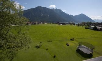 A large green meadow with mountains in the background. In the foreground is a trampoline.