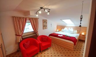 A cozy bedroom with a large bed and red seating. Bright colors and a sloping roof create an inviting atmosphere.