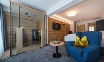 A modern room with wooden walls and a cozy blue armchair. A glass shower and a small table with a flower complement the stylish decor.