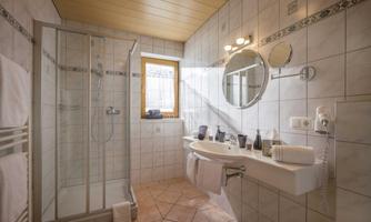 A modern bathroom with a shower, sink, and mirror. Brightly tiled with natural light sources from a window.