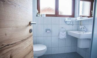 A modern bathroom with white tiles and large windows. It is simply and brightly designed with a sink and a toilet.