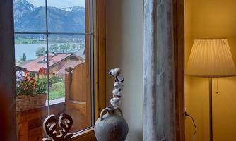 A window view of a picturesque landscape with mountains and a lake. In the foreground, there is a lamp and a decorative vase.