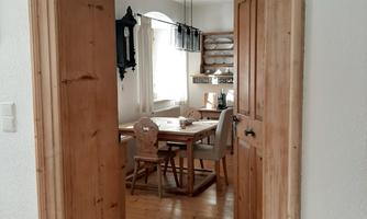 An inviting room with wood details and a table. The view through the door frame reveals cozy furnishings and natural light.