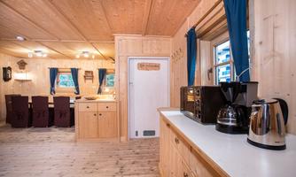 A cozy wooden kitchen with modern appliances and a dining area. Bright windows with blue curtains create a friendly atmosphere.